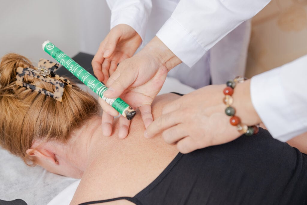 Therapeut führt Moxibustion durch, hält angezündete Moxa-Zigarre über Akupunkturpunkt zur Tiefenwärmebehandlung und Förderung des Qi-Flusses.